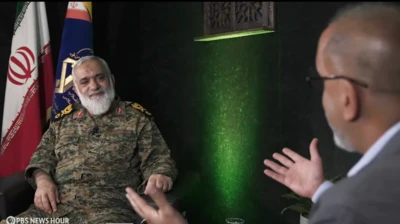 محمدرضا نقدی، مشاور عالی فرمانده کل سپاه پاسداران روی صندلی در برابر دوربین پی‌بی‌اس نشسته است