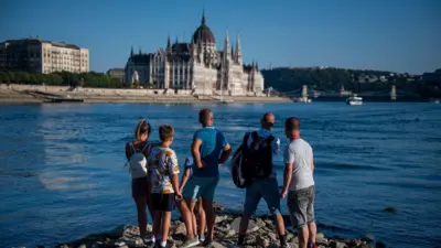 Az emberek a Dunát figyelik, amely rekordalacsony vízállással folyik Budapest belvárosában 2026. július 28-án. A folyó vízmércéje július 28-án 31 centimétert mutatott a magyar Országos Vízügyi Főigazgatóság szerint.