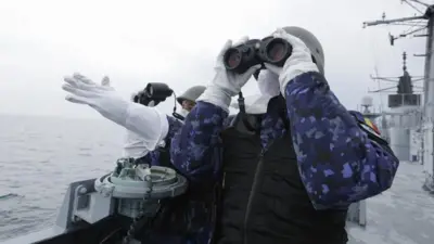 フリゲート艦の甲板で兵士2人が双眼鏡を手に監視している