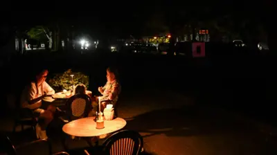 Две женщины сидят на открытой террасе ресторана в Севастополе во время отключения уличного освещения 22 июля 2026 года