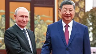 Putin w ciemnym garniturze, białej koszuli i krawacie w groszki ściska dłoń Xo w granatowym garniturze, czerwonym krawacie i białej koszuli. Obaj przywódcy spotykają się na ceremonii parzenia herbaty.