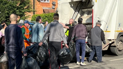 People queue to get their rubbish in a bin lorry, with police officer in centre