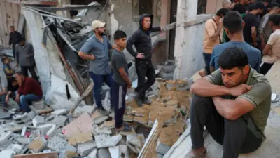 A man sits as Palestinians gather at the site of an Israeli strike on a house in Gaza. 