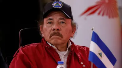 Daniel Ortega, de boné e jaqueta vermelha, ao lado de uma pequena bandeira da Nicarágua