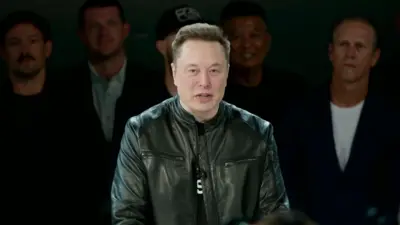 Elon yambaye ijaketi y'uruhu y'umukara, arimo kuvuga. 