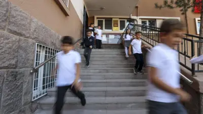Bir okul merdiveninden aşağıda doğru koşan çocuklar. 
