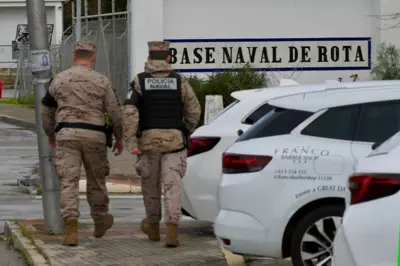 Militares vistos de espalda caminan cerca de autos blancos en la Base Naval de Rota