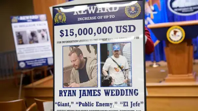 A reward poster for the arrest of Ryan James Wedding is visible following a news conference announcing the indictment of a former Olympic snowboarder Ryan Wedding, charging him with murder and money laundering in connection to a drug trafficking organization at the Justice Department on November 19, 2025 in Washington, DC.