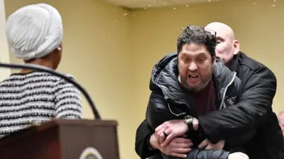 A photo of Olhan Omar addressing a town hall meeting while speaking into a microphone at a podium