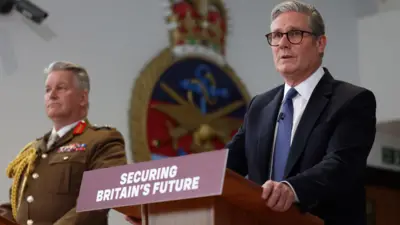 UK Prime Minister Keir Starmer in a suit, accompanied by General Sir Jim Hockenhull in military uniform standing at podiums with a sign that reads 'Securing Britain's Future'
