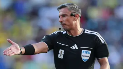 El árbitro Slavko Vinčić levanta su brazo derecho mientras dirige un partido