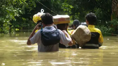ကျောလယ်အထိမြင့်တက်နေတဲ့ ရေတွေကြား အထုပ်တွေ၊ မာမားခေါက်ဆွဲဘူးတွေကို ခေါင်းပေါ်ရွက်ကာ ကူညီရေးသွားနေတဲ့ ရခိုင်လူငယ်တွေ