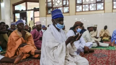 Olujọsin kan wọ agbada funfun, o de fila buluu niwaju awọn olujọsin mii tawọn naa wọ oriṣiiriṣii aṣọ buba