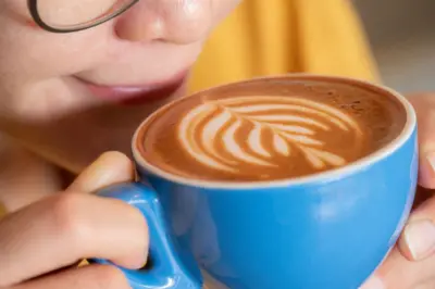 woman sips a milky coffee from a blue cup