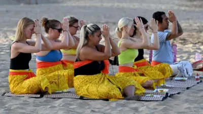 Wisatawan asing berpartisipasi dalam acara doa Hindu Bali di sebuah pantai di Seminyak dekat Denpasar di pulau wisata Bali.