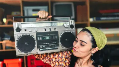 صورة لشابة تبدو سعيدة وهي تحمل على كتفها جهاز مسجل الكاسيت