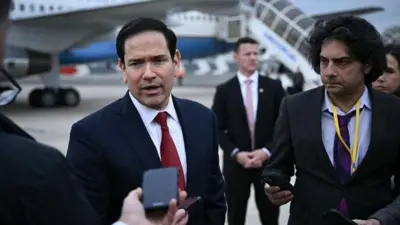 Marco Rubio falando a jornalistas em aeroporto com aeronave ao fundo