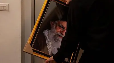 یک مرد که از پشت سر دیده‌می شود قاب عکس علی خامنه‌ای را در دست دارد.