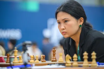 21-летняя шахматистка Бибисара Асаубаева в черном пиджаке склонилась над шахматной доской