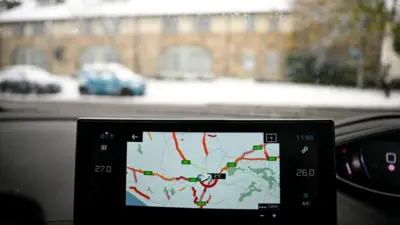 Спутниковый навигатор в машине на фоне заснеженного пейзажа.