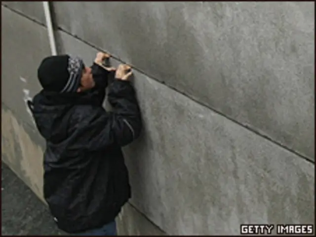 Un joven intenta mirar a través de una grieta en lo que queda del Muro de Berlín