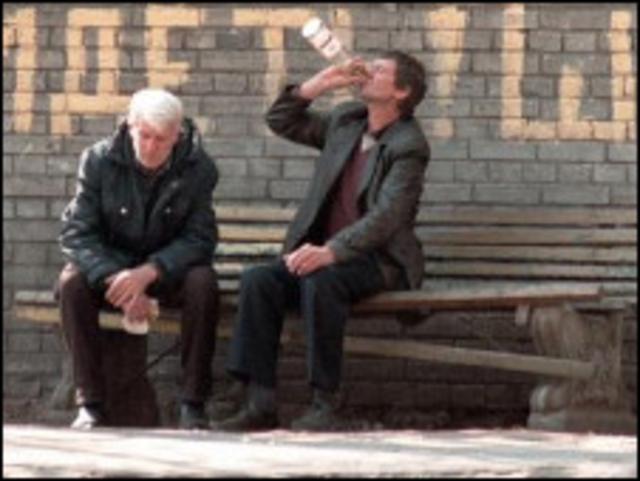 Двое мужчин, сдия на скамейке, пьют водку 