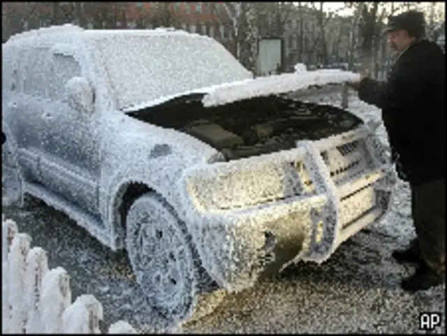 Мужчина поливает водой оледеневшую машину в России (архивное фото)