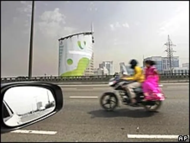 印度古尔冈一对男女骑着摩托车飞驰驶过一座商业大楼（4/3/2010）