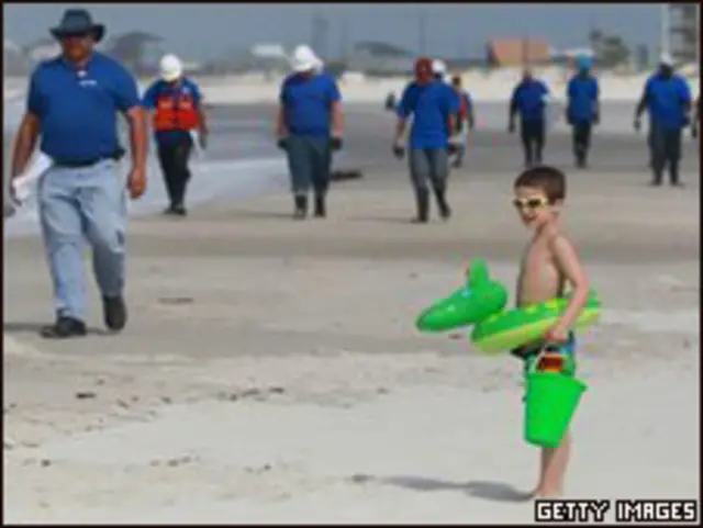 Niño observa a trabajadores recoger desechos petroleros en playa de Alabama.