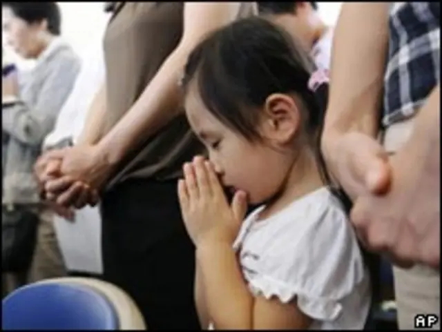 تصویری کودکی ژاپنی که در میان بزرگسالان به نیایش مشغول است