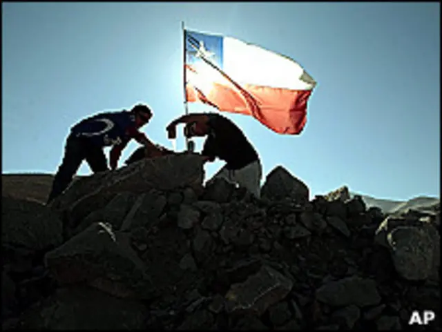 Dos hombren colocan una bandera de Chile sobre la mina.