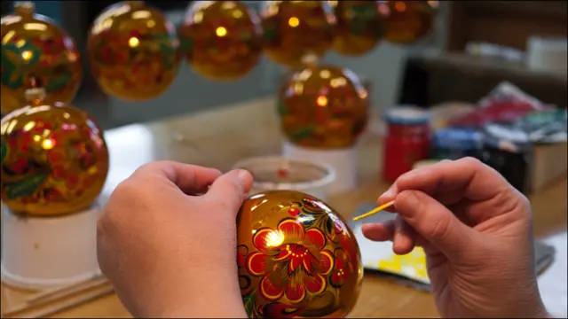 Художница расписывает елочный шар под хохлому