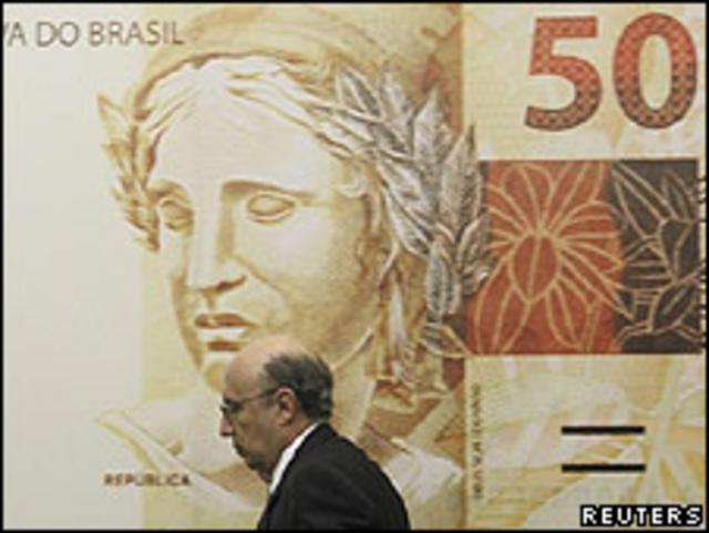 El presidente del Banco Central de Brasil, Henrique Meirelles, pasa por delante de un billete gigante