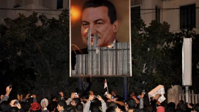 मिस्र के पूर्व शासक होस्ने मुबारक की तस्वीर के सामने प्रदर्शन करते सरकार विरोधी लोग.