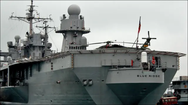 Khu vực boong tàu của tàu Blue Ridge trông rộng rãi và sạch sẽ. Bên rìa boong là một chiếc trực thăng tầm trung đang đậu sẵn. 