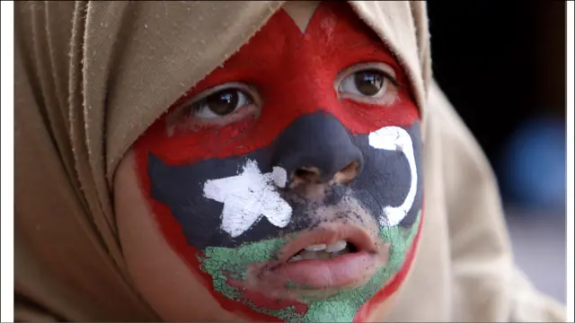 بن غازی شہر میں مظاہرے کے دوران ایک بچی نے اپنے چہرے پر لیبیا کے پرانے پرچم کو رنگ لیا ہے۔