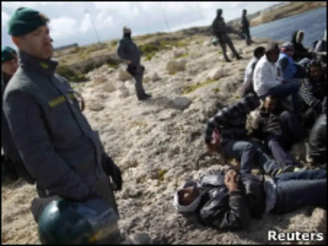 Tunisianos são observados por soldados italianos em Lampedusa.