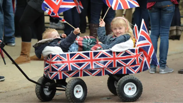 Dua bocah kecil ini tiba di kawasan prosesi pernikahan dengan kereta tarik lengkap dengan bendera nasional Inggris, Union Jack.