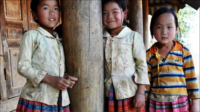 Các em bé gái Hmong xinh xắn xúng xính trong bộ váy thổ cẩm của dân tộc mình thì chơi trên thềm nhà, e thẹn khi ống kính của tôi lia về phía em. 