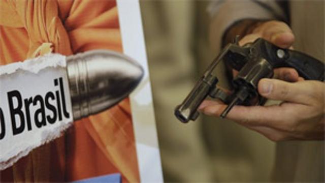 Un hombre sostiene un revólver junto a un cartel en el primer día de una campaña de desarme en Brasil.