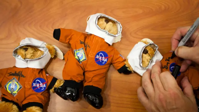 Salah satu kru pesawat menandatangani boneka beruang astronot dengan logo NASA dan Atlantis. 