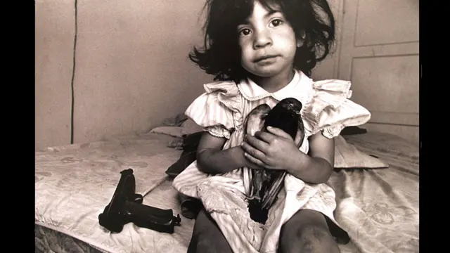 “Conocí las pandillas de Los Angeles cuando escribía un reportaje sobre el HIV en El Salvador en 1990. Un doctor me posibilitó fotografiar el ala de SIDA del hospital público y cuando entró alguien gritó: ‘¡Hey! Finalmente alguien de mi país’. Y yo le respondí: ¿Qué país es ese? Y Franklin Torres respondió: ‘Los Angeles’. Franklin tenía tatuajes de la cabeza a los pies. Era miembro de la 18 de Los Angeles y había sido deportado a El Salvador. Nunca había visto a alguien como Franklin antes. No había pandillas en El Salvador durante los años 80 cuando cubrí la guerra. Por eso, conocer a Franklin me abrió los ojos a realidades dentro de mi propio país”. En esta foto una niña en una casa en Los Angeles. 