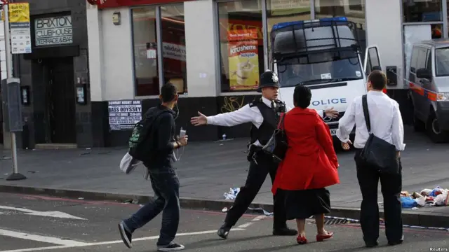 Полицейский заграждает дорогу пешеходам, проходящим мимо бойни в Брикстоне