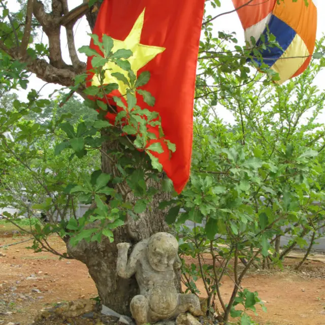 Cờ đỏ sao vàng và cờ Phật giáo cắm ở một gốc cây, phía dưới là ngạ quỷ (quỷ đói) chịu hình phạt.
