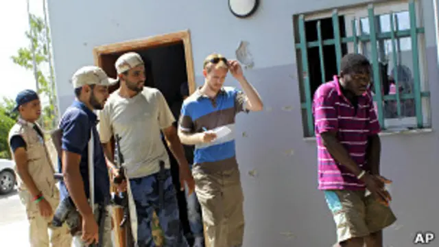 Ливийские повстанцы и иностранный журналист смотрят на темнокожего африканца, задержанного по подозрению в наемничестве (28 августа 2011 года)