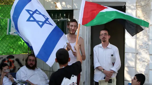 Seorang anak Palestina mengibarkan bendera Palestina di hadapan pemukim Yahudi