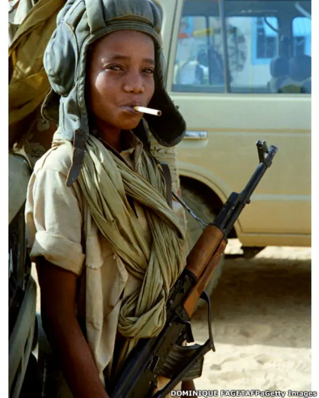 1987 йилнинг 5 апрели. Ливия билан Чад ўртасида келиб чиққан ҳарбий можародан кейин Ливия армияси чекинган. Қалаитда суратга олинган чадлик бола жангчи қўлида АК-47 автомати, Совет танкчиси бош кийими ва оғзида сигарет билан ғалабани нишонлаяпти. 