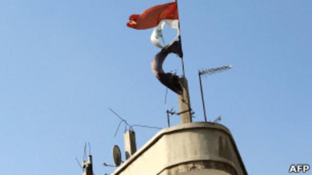 Разорванный сирийский флаг развевается над зданием в Хомсе