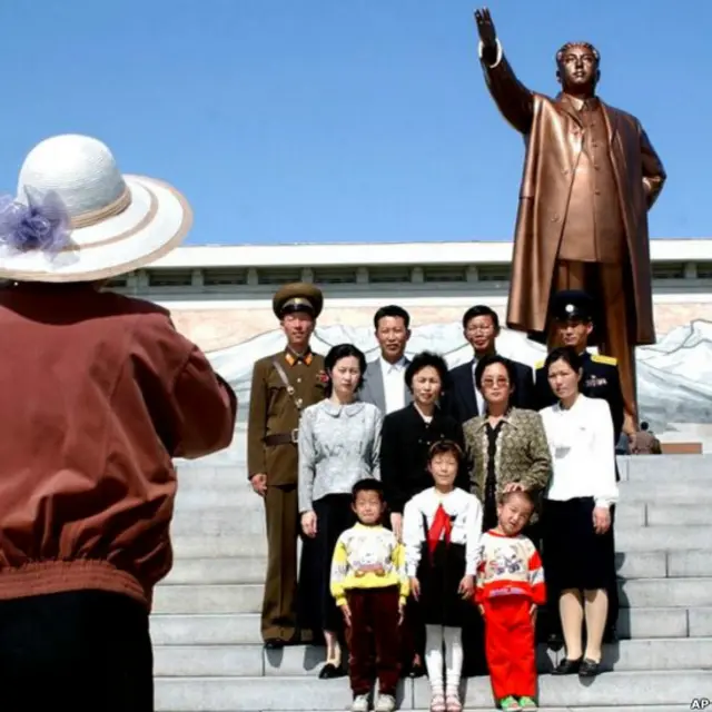 Tuy nhiên đây là cuộc sống dưới bóng của cố Chủ tịch Kim Il-sung. Trên ảnh là một gia đình Bắc Hàn chụp hình kỷ niệm nhân ngày lễ Lao động trước tượng Lãnh tụ Vĩ đại tại Bình Nhưỡng, 1/5/2002. 