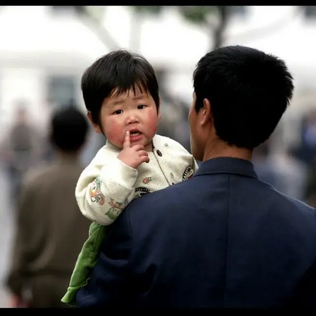 Mặc dù khó khăn nhưng người dân Bắc Hà vẫn có cuộc sống của mình. Đây là một người cha bồng con trên đường phố Bình Nhưỡng, tháng 5/ 2001. 